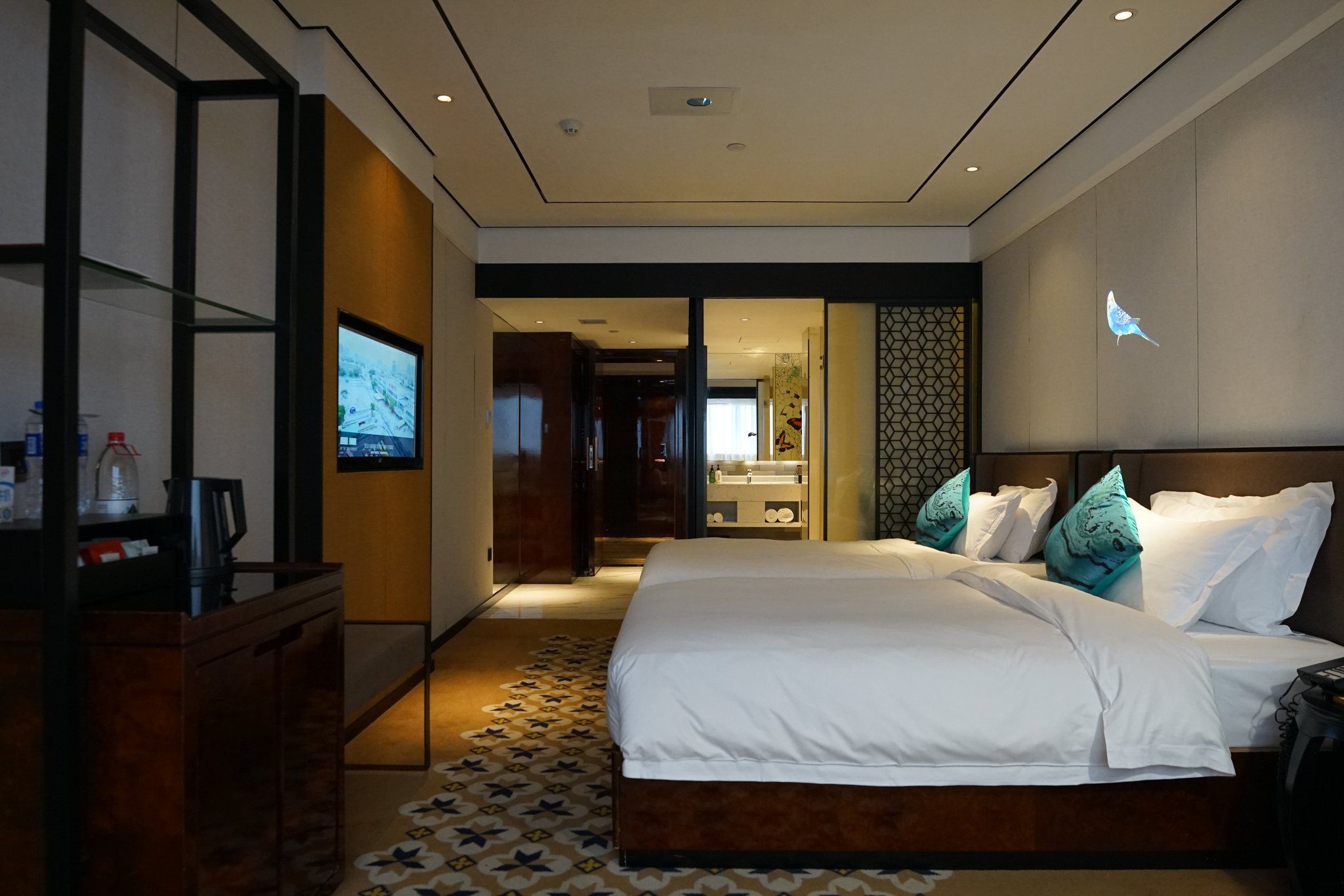 Une chambre d’hôtel moderne, dotée d’un grand lit, d’une télévision et d’une salle de bain visible à travers une porte ouverte.
