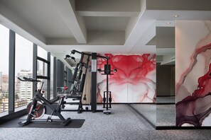 Academia moderna com equipamentos de exercício, bicicleta ergométrica e uma grande pintura abstrata na parede.