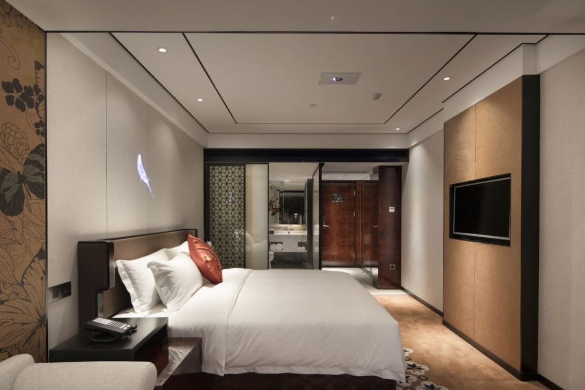 Een moderne hotelkamer met een groot bed, een flatscreen televisie, een nachtkastje en een kamerkleed met dessin.