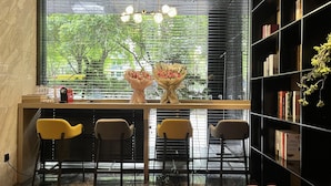 Un interior moderno con un escritorio de madera, tres sillas, una estantería y una ventana con persianas.
