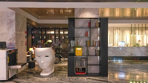 Um hall de entrada com piso de mármore, uma grande escultura branca, um balcão de recepção com computadores e uma estante repleta de livros.