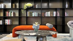 Una sala de estar moderna con una mesa de centro de mármol redonda, un sofá naranja y una estantería llena de libros.