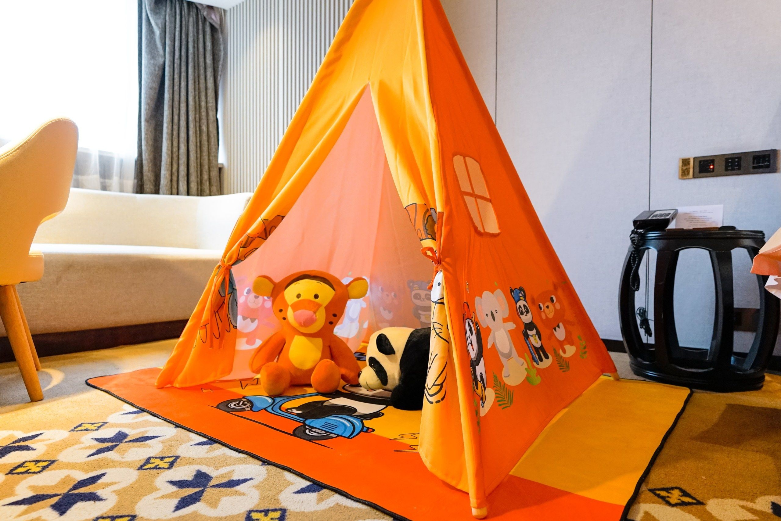 Quarto com uma tenda infantil para brincar com personagens de desenho animado, um sofá, uma mesa de centro e um tapete estampado.