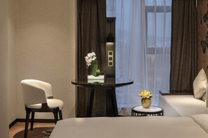 Una habitación de hotel con una cama, una mesa redonda con un jarrón de flores, una silla y un sofá.