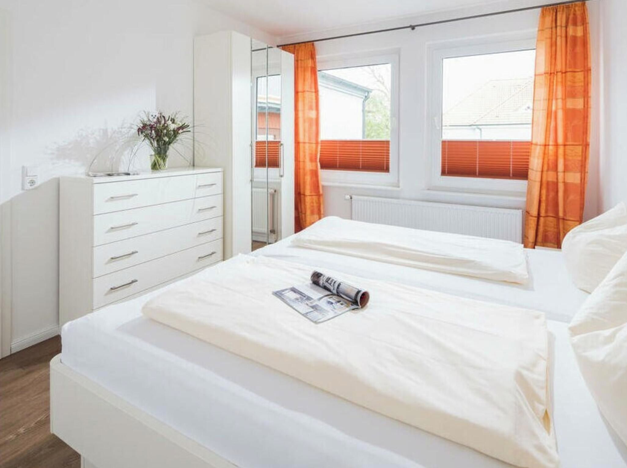 A bedroom with two beds, a dresser, a mirror, and a window with curtains.