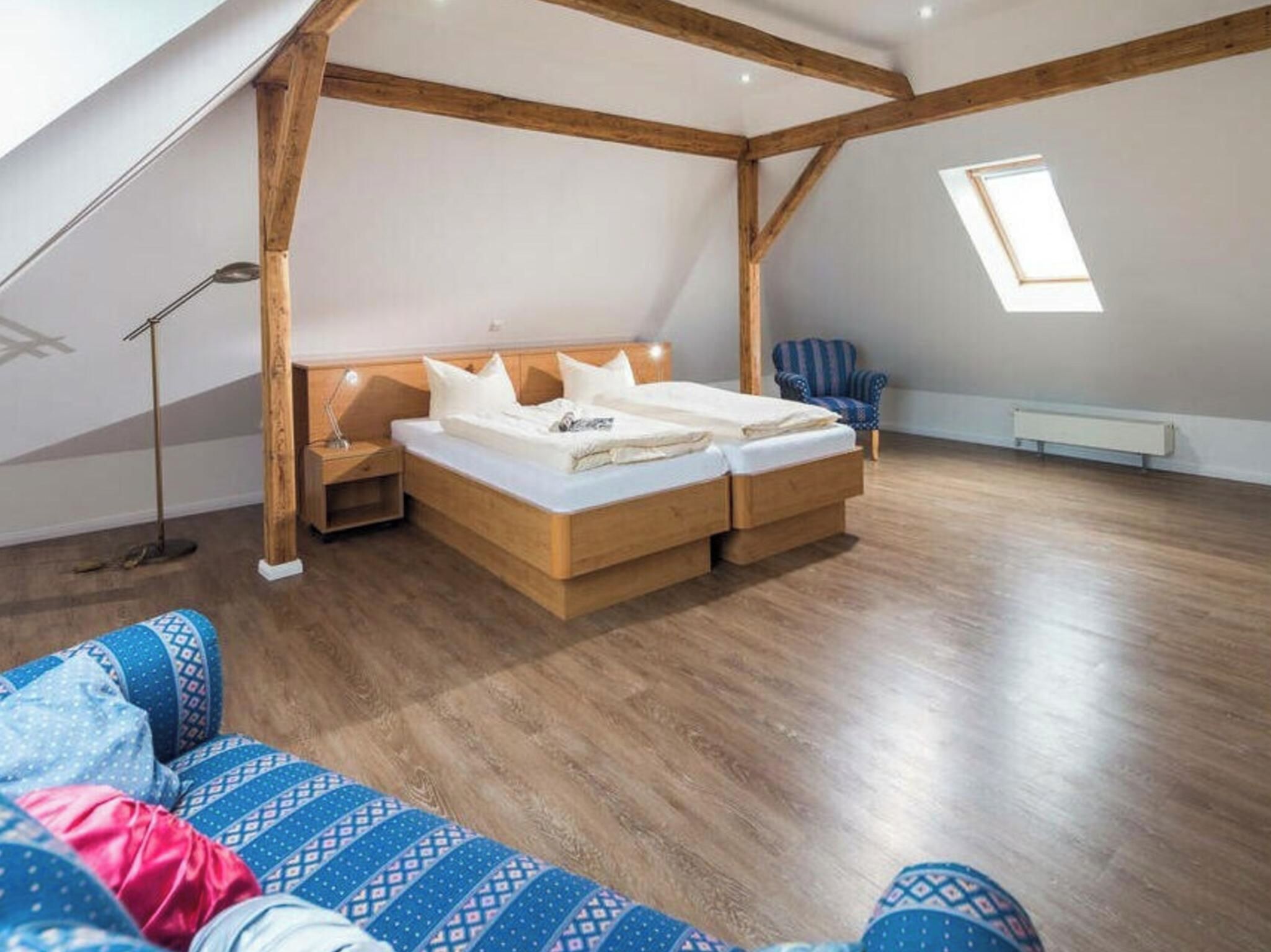 A bedroom with a wooden ceiling, a bed, a nightstand, a chair, and a window.