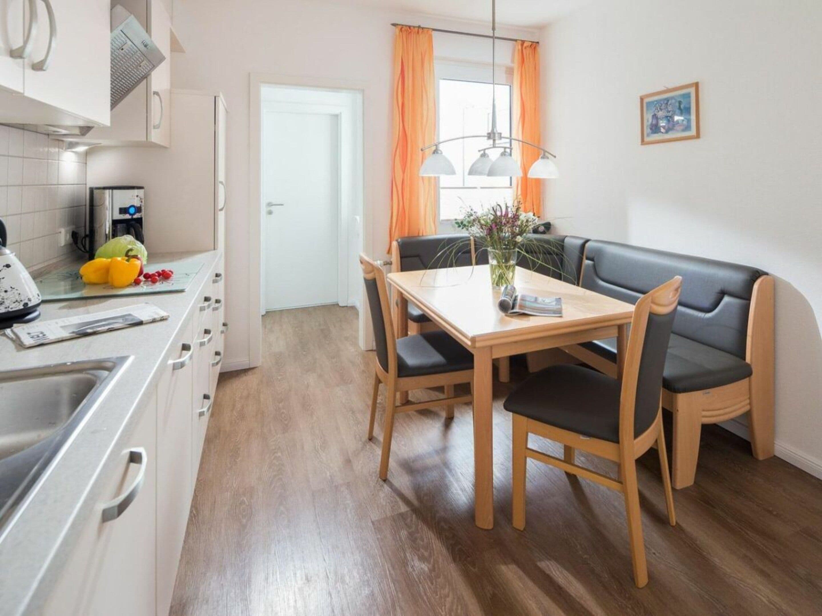 Une cuisine compacte avec un coin repas, comprenant une table en bois, des chaises et un banc en cuir noir.