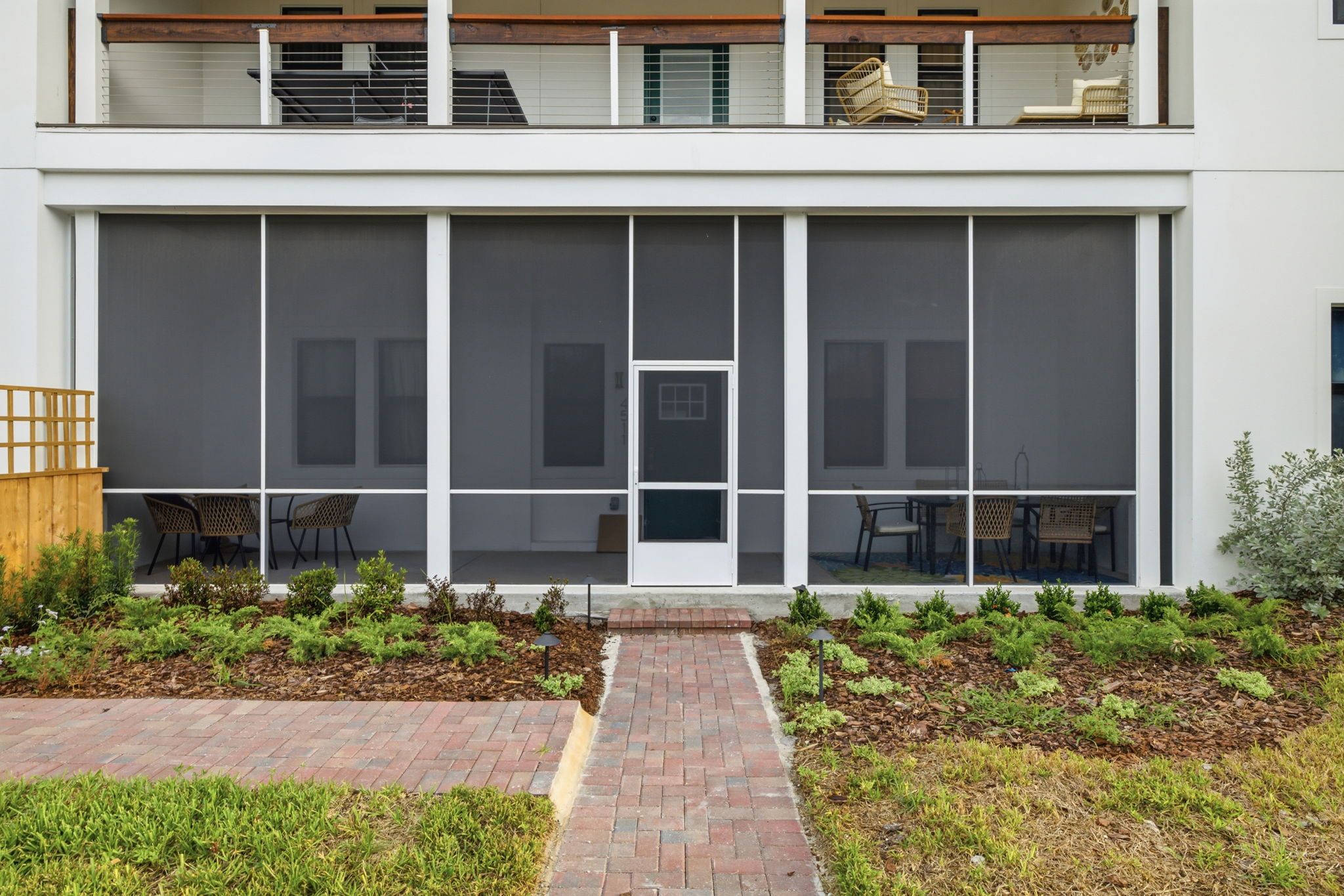 A modern building with a large glass facade, a central entrance, and a brick pathway leading to a seating area with outdoor furniture.