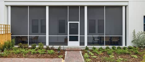 A modern building with a large glass facade, a central entrance, and a brick pathway leading to a seating area with outdoor furniture.