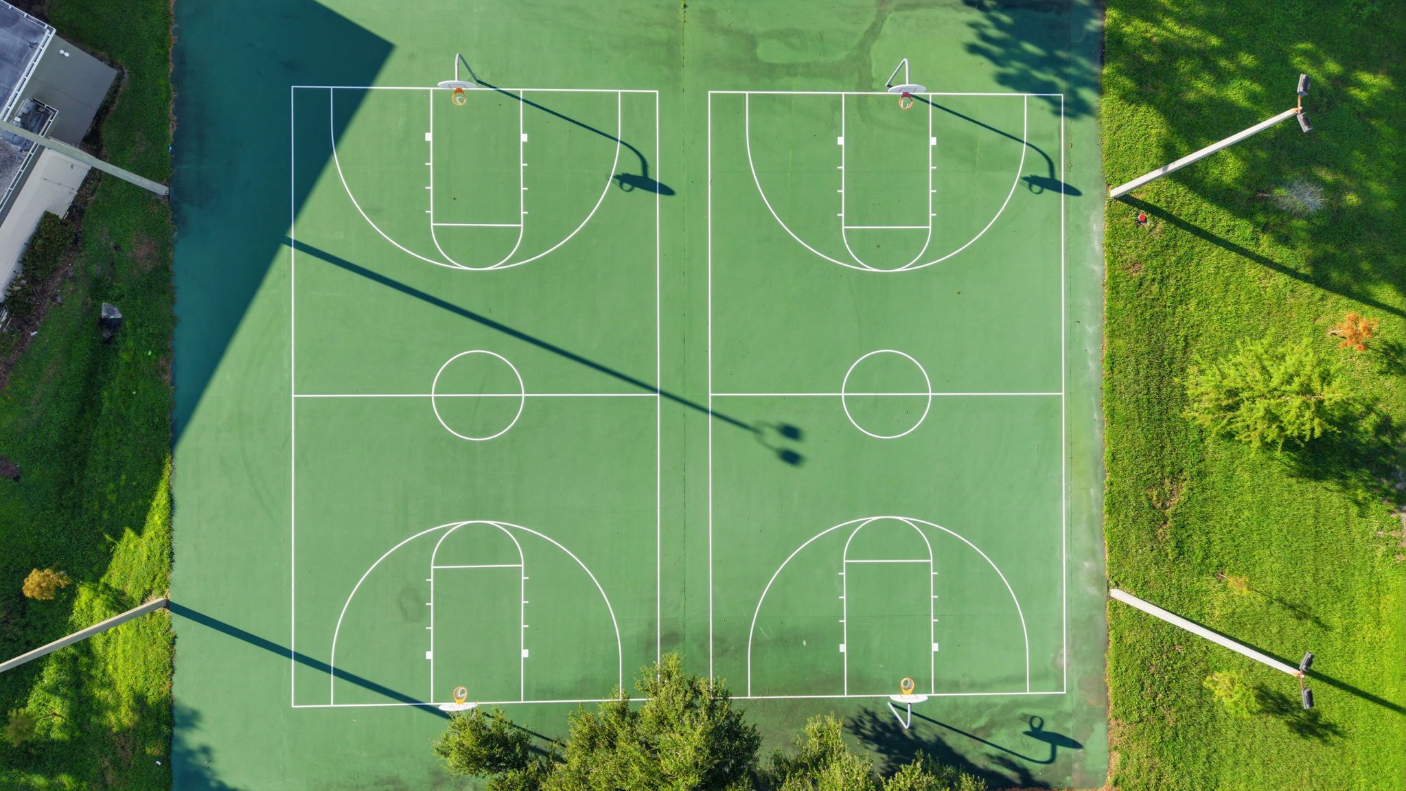 A basketball court with four hoops, surrounded by grass and trees.