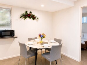 Un coin repas avec une table ronde, des chaises grises, un vase de fleurs et un four à micro-ondes posé sur une étagère.