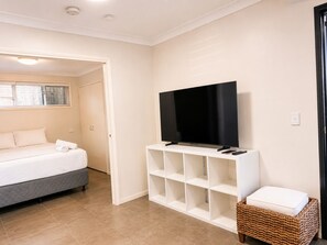 A hotel room with a bed, a television on a white stand, and a wicker basket. - 1Bed 1Bath Ground floor West End (West End)