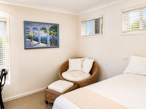 A bedroom with a bed, a wicker chair with cushions, a wall-mounted painting, and a window with blinds. - 1Bed 1Bath Ground floor West End (West End)