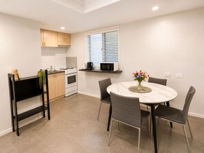 Une cuisine moderne avec des meubles blancs, une cuisinière et un four à micro-ondes. On y trouve une table à manger avec des chaises et un vase rempli de fleurs.