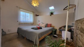 Quarto com cama, mesa de cabeceira, abajur, planta e janela.