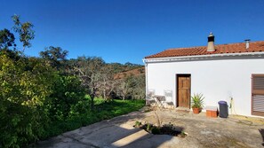 A white building with a tiled roof, a wooden door, and a small garden area with plants and a bench. - Casa Aurora- A Restful Home Beneath Starry Skies (São Martinho das Amoreiras)