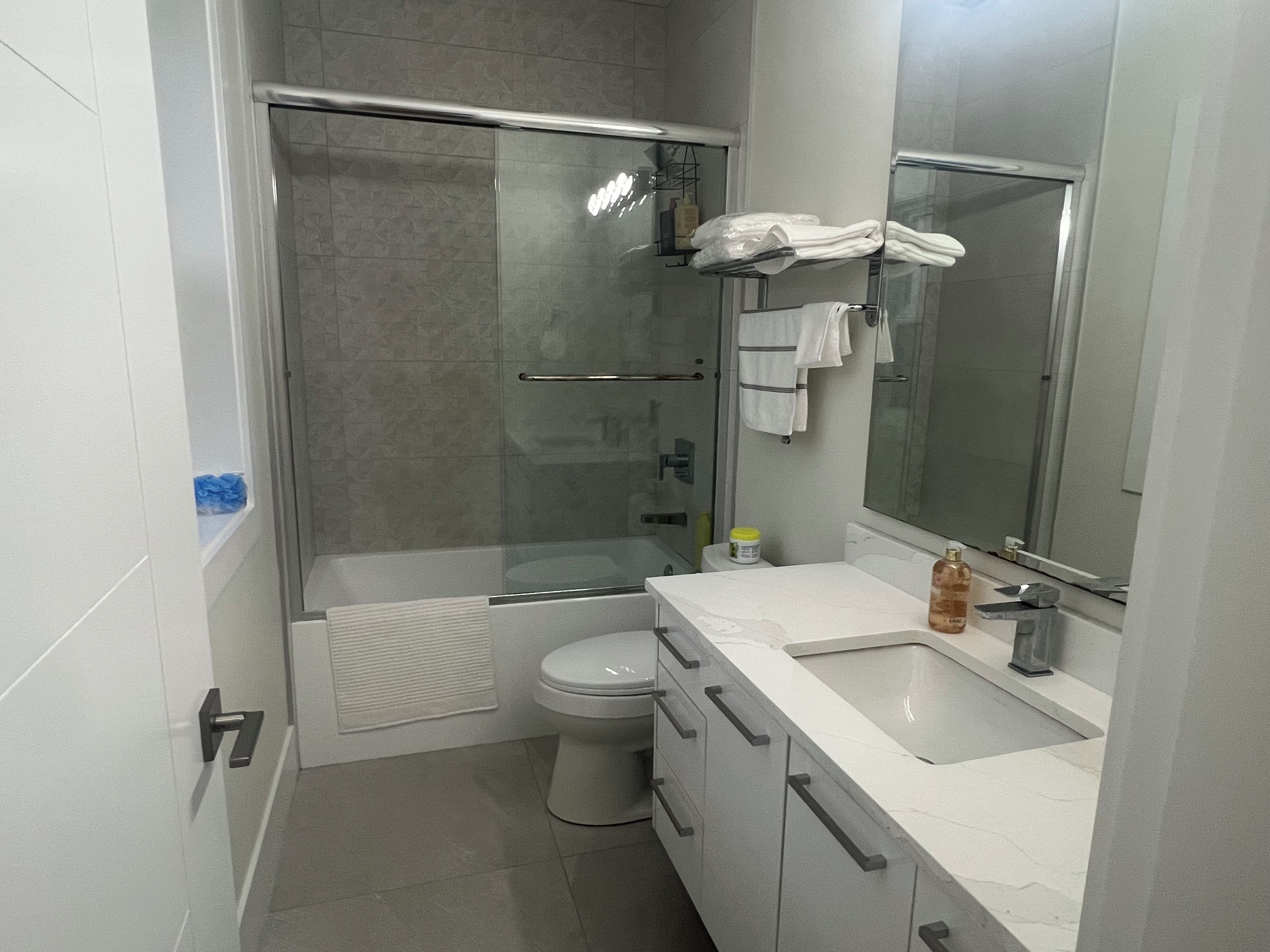 Un baño moderno con ducha envuelta en vidrio, inodoro, lavamanos con espejo y toallero.