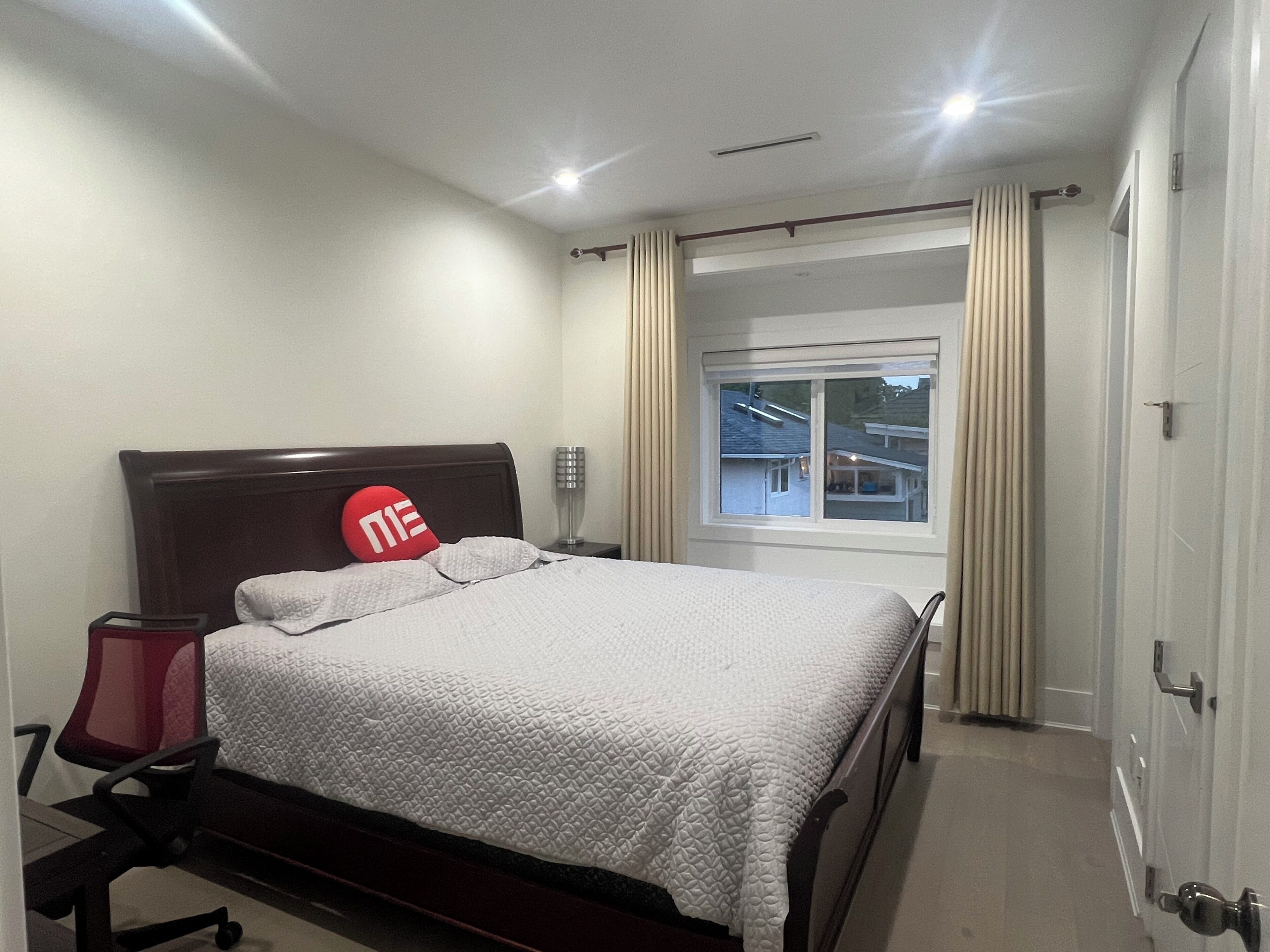 Une chambre d’hôtel avec un lit, une table de chevet, un fauteuil rouge, une fenêtre avec des rideaux et une vue sur l’extérieur.
