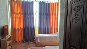 Una habitación con piso de madera, una cama con colchón blanco, una mesita de noche de madera y una puerta con detalles decorativos tallados.