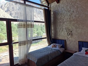 Een kamer met een bed, een raam met gordijnen en uitzicht op een bergachtig landschap.