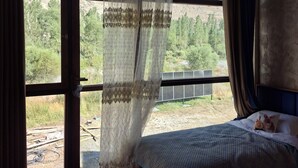 Un dormitorio con un ventanal grande, una cama con cubrecama azul y vistas a un paisaje montañoso.