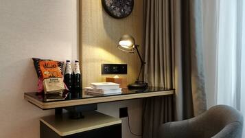 A hotel room with a desk, a lamp, a chair, and a wall clock.