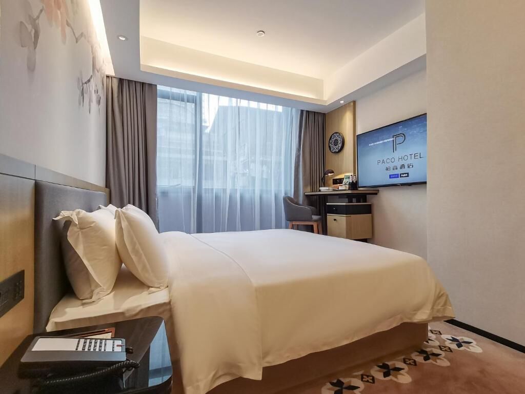 Een hotelkamer met een bed, een bureau, een stoel, een televisie en een raam met gordijnen.