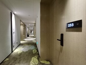 Un pasillo de hotel con piso alfombrado, una puerta con letrero de número y un picaporte.