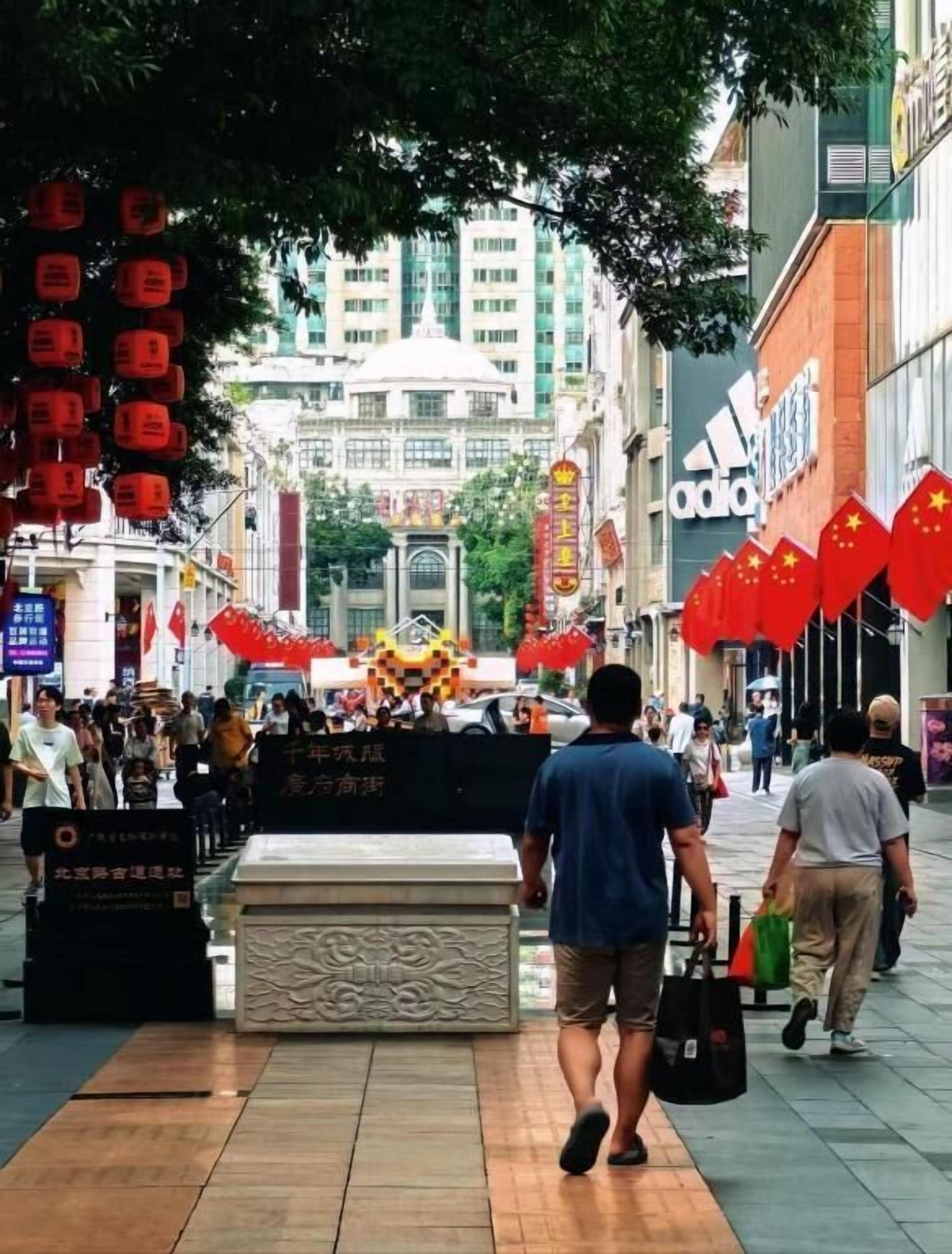 A busy urban street with pedestrians, a monument, and commercial buildings.