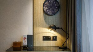 Un escritorio con una lámpara, una caja de pañuelos, un plato decorativo y un panel de control en la pared.