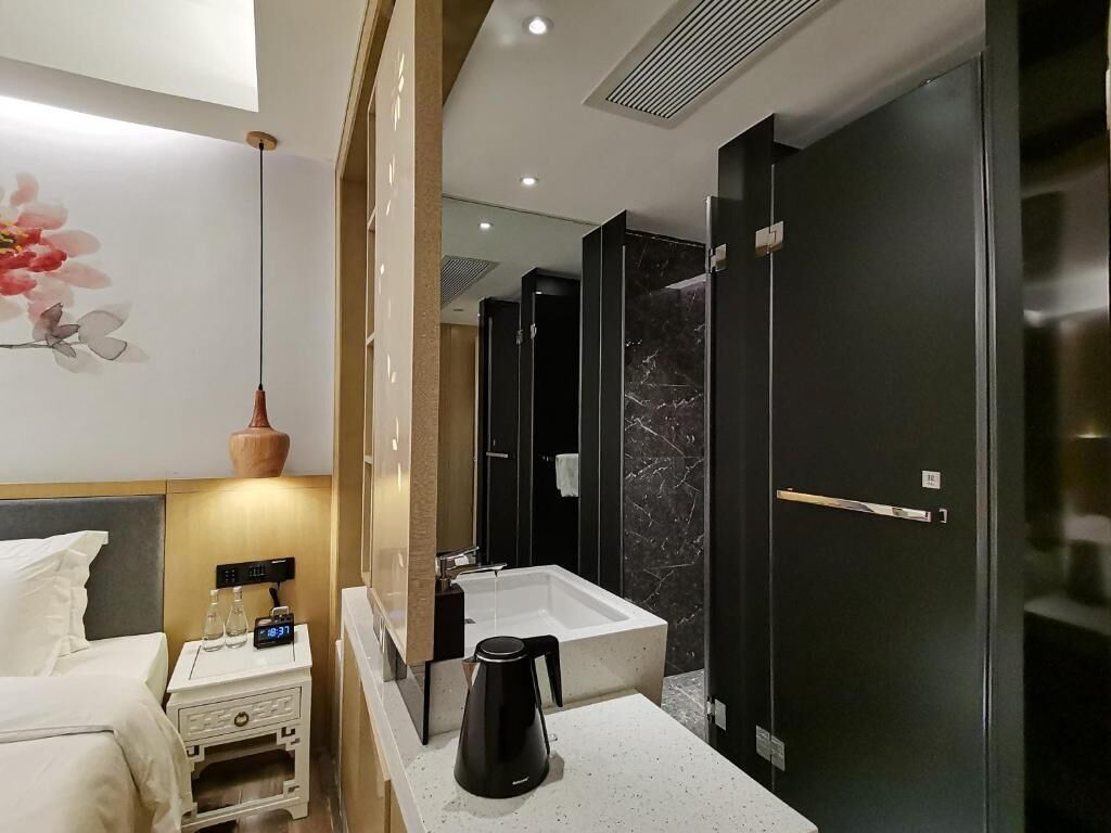 A modern bathroom with a large mirror, a white sink, a black coffee maker, and a dark door.