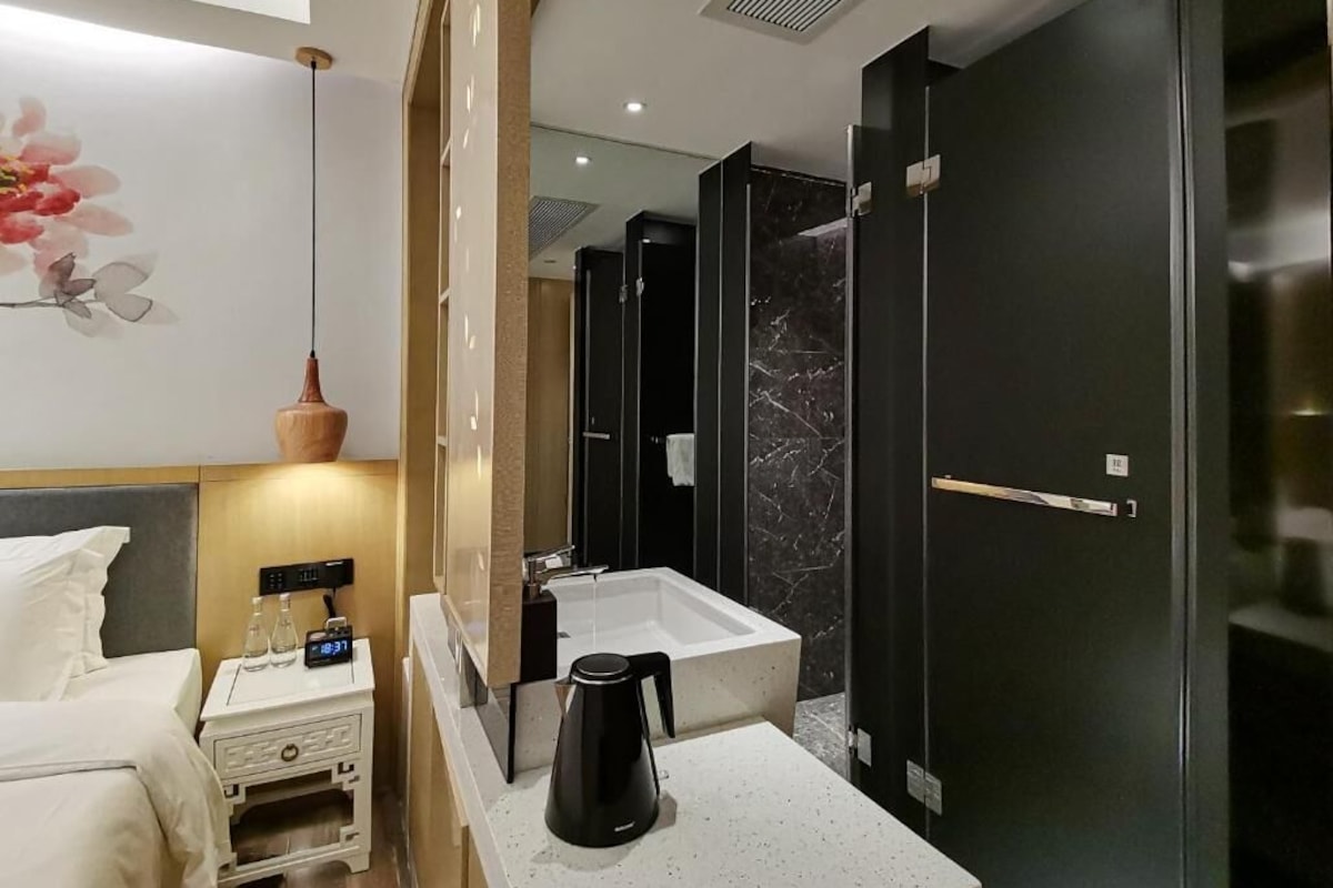 Un baño moderno con un espejo grande, un lavamanos blanco, una cafetera negra y una puerta oscura.