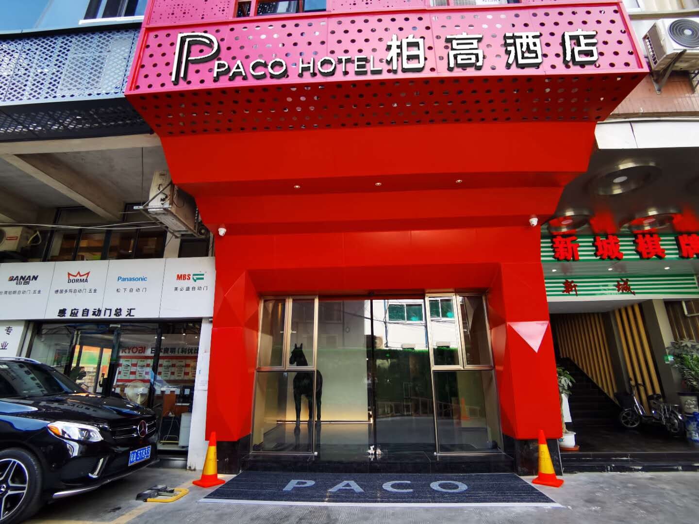 The entrance to Paco Hotel with a prominent red awning and a black car parked in front.