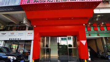 The entrance to Paco Hotel with a prominent red awning and a black car parked in front.