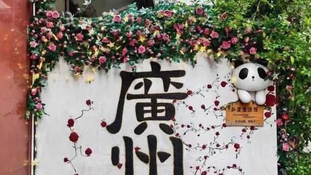 Una pared con caracteres chinos y un adhesivo de panda, rodeada de follaje.