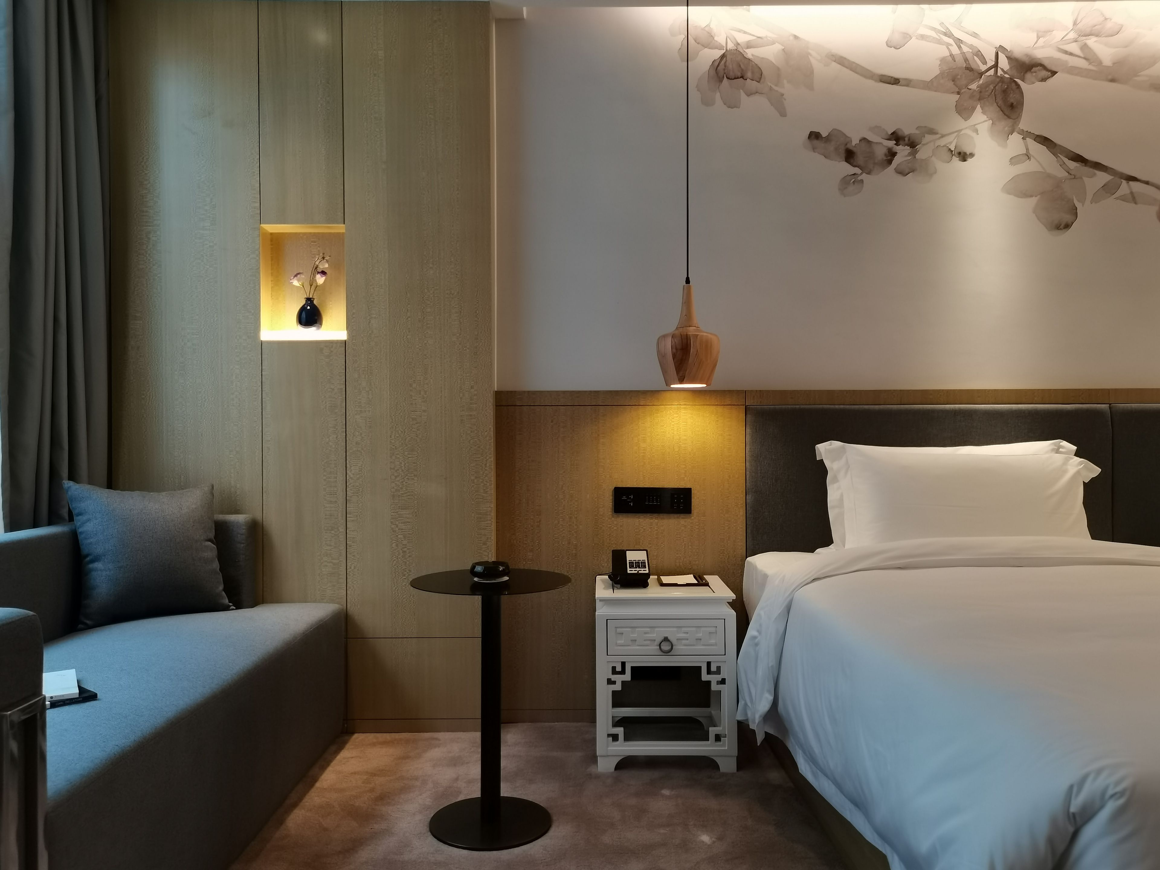 Una habitación de hotel con cama, mesita de noche, lámpara y una lámpara de pared.