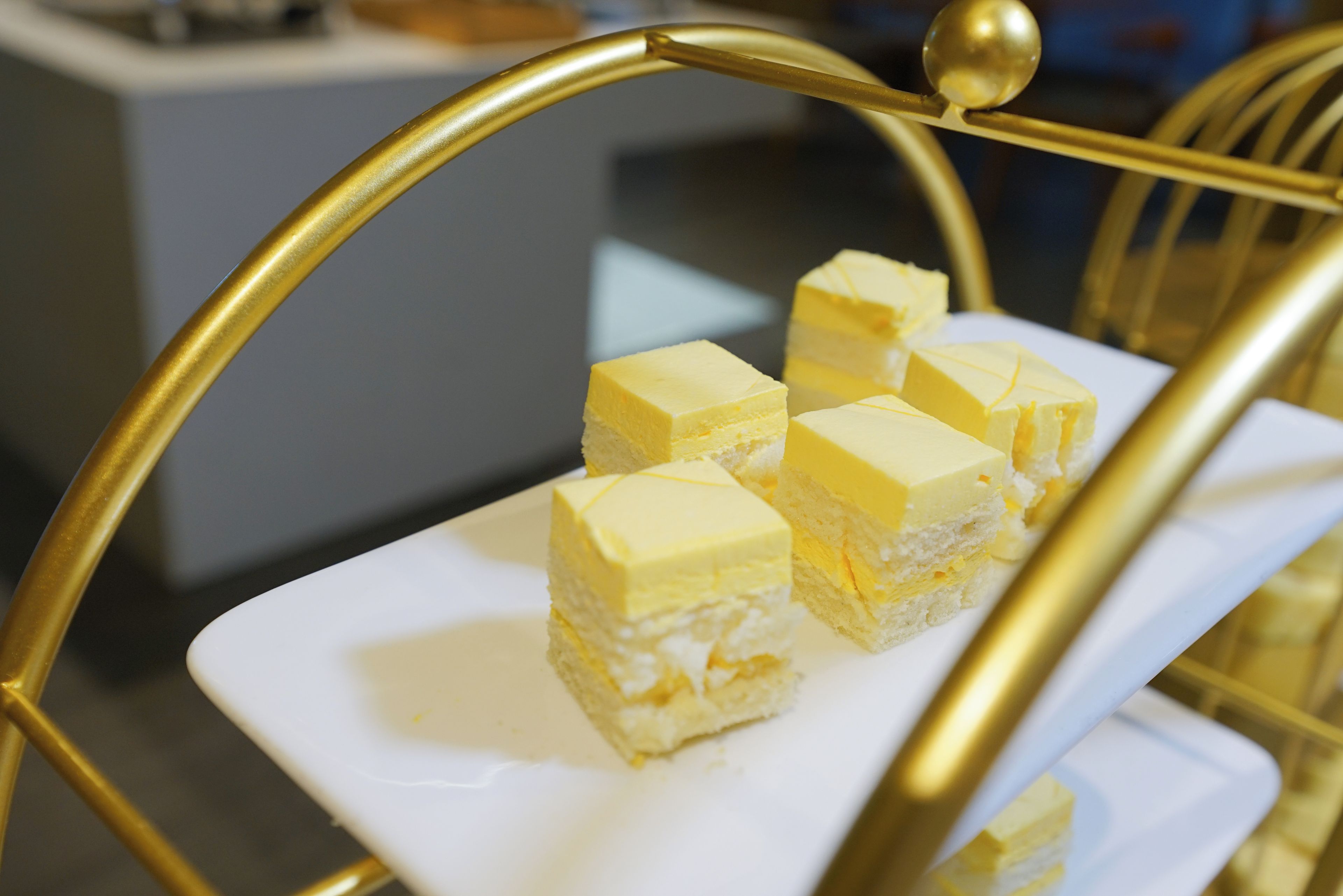 En vit, rektangulär tallrik med flera kvadratiska bitar av gul dessert, placerade på ett gyllene fat.