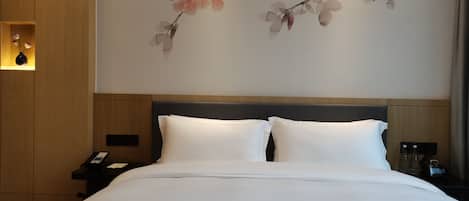A hotel room with a bed, a nightstand, a wall-mounted clock, and a floral artwork.