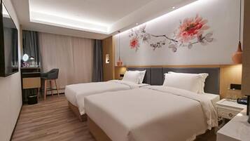 A hotel room with two beds, a desk with a chair, a large floral artwork on the wall, and a bedside table with a lamp.