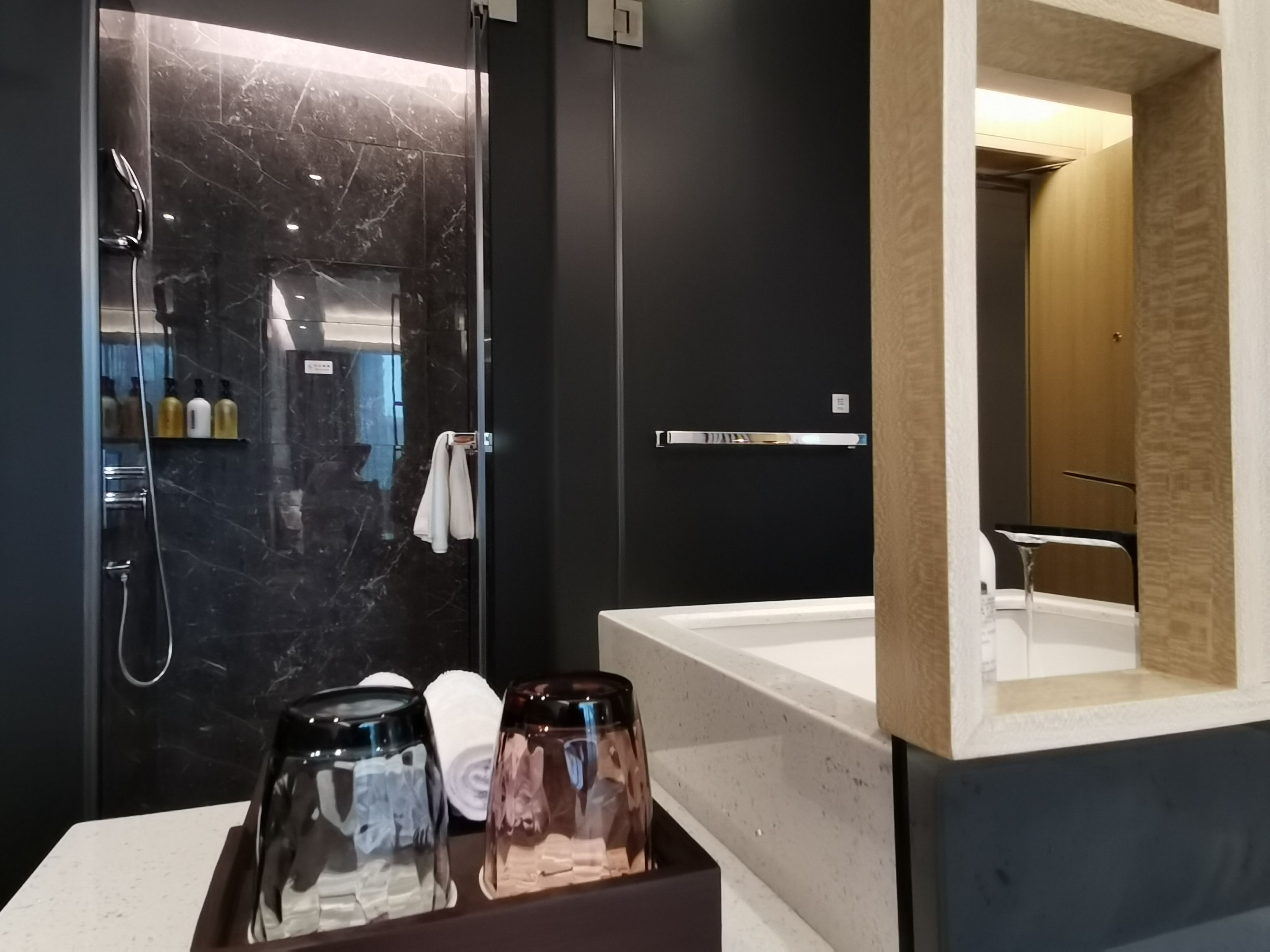 A modern bathroom with a marble shower, a bathtub, and a vanity with toiletries.