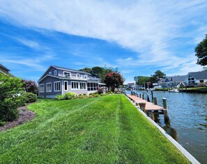 Une propriété située au bord de l’eau, dotée d’une pelouse bien entretenue, d’une jetée s’avançant dans l’eau et d’une maison avec un toit à pignon.