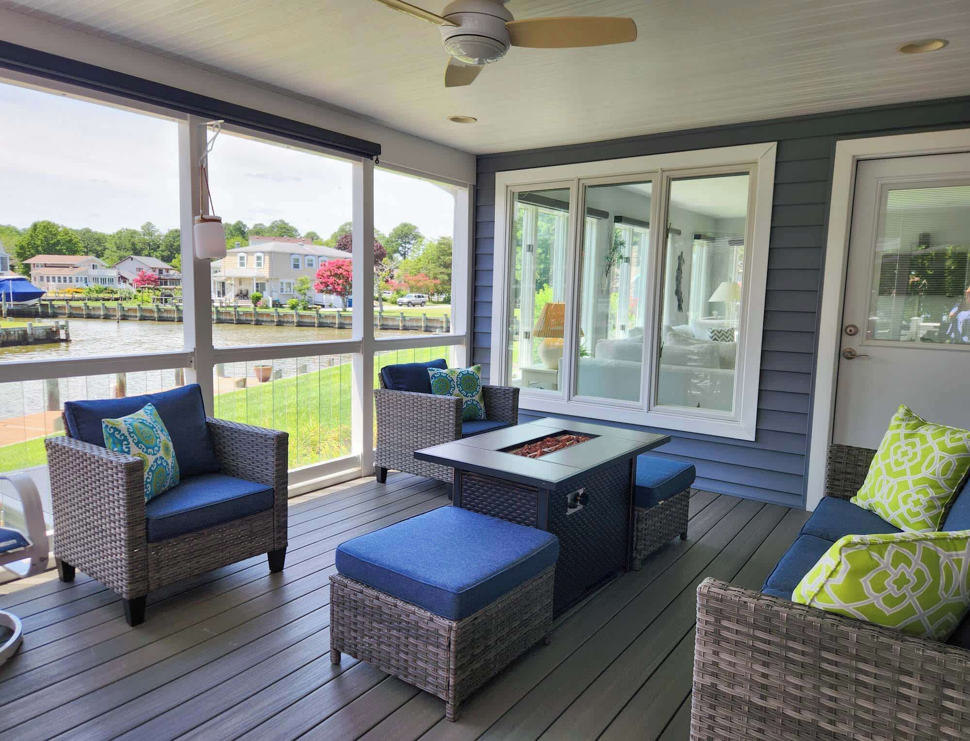 A covered outdoor deck with wicker furniture, a table, and a view of a residential area.