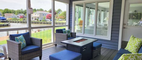 A covered outdoor deck with wicker furniture, a table, and a view of a residential area.