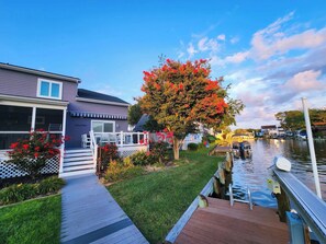 A waterfront property with a dock, a covered outdoor seating area, and a well-maintained garden with flowering plants. - The Cove at Ocean Pines | Boater’s Paradise (Ocean Pines)