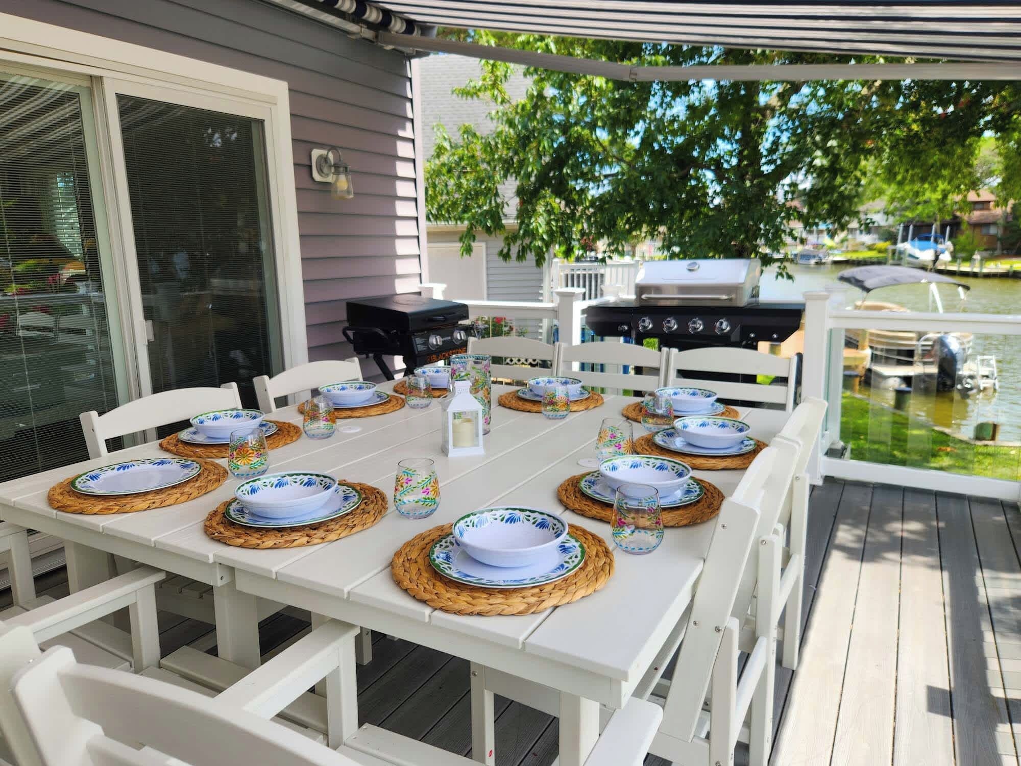 An outdoor dining area with a white table set for six, surrounded by white chairs.
