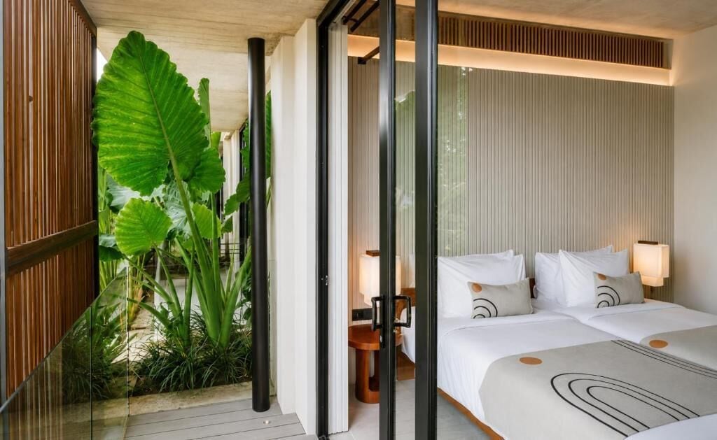 Une chambre d’hôtel avec un lit, des tables de chevet, une petite table et une vue sur un jardin tropical.