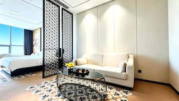 A modern hotel room with a bed, a white sofa, a round coffee table, and a patterned rug.