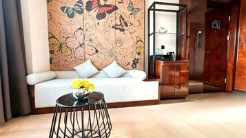 Een hotel lobby met een bank, een ronde tafel met een bloevas, een decoratieve wand met bloemenmotieven en een lift.