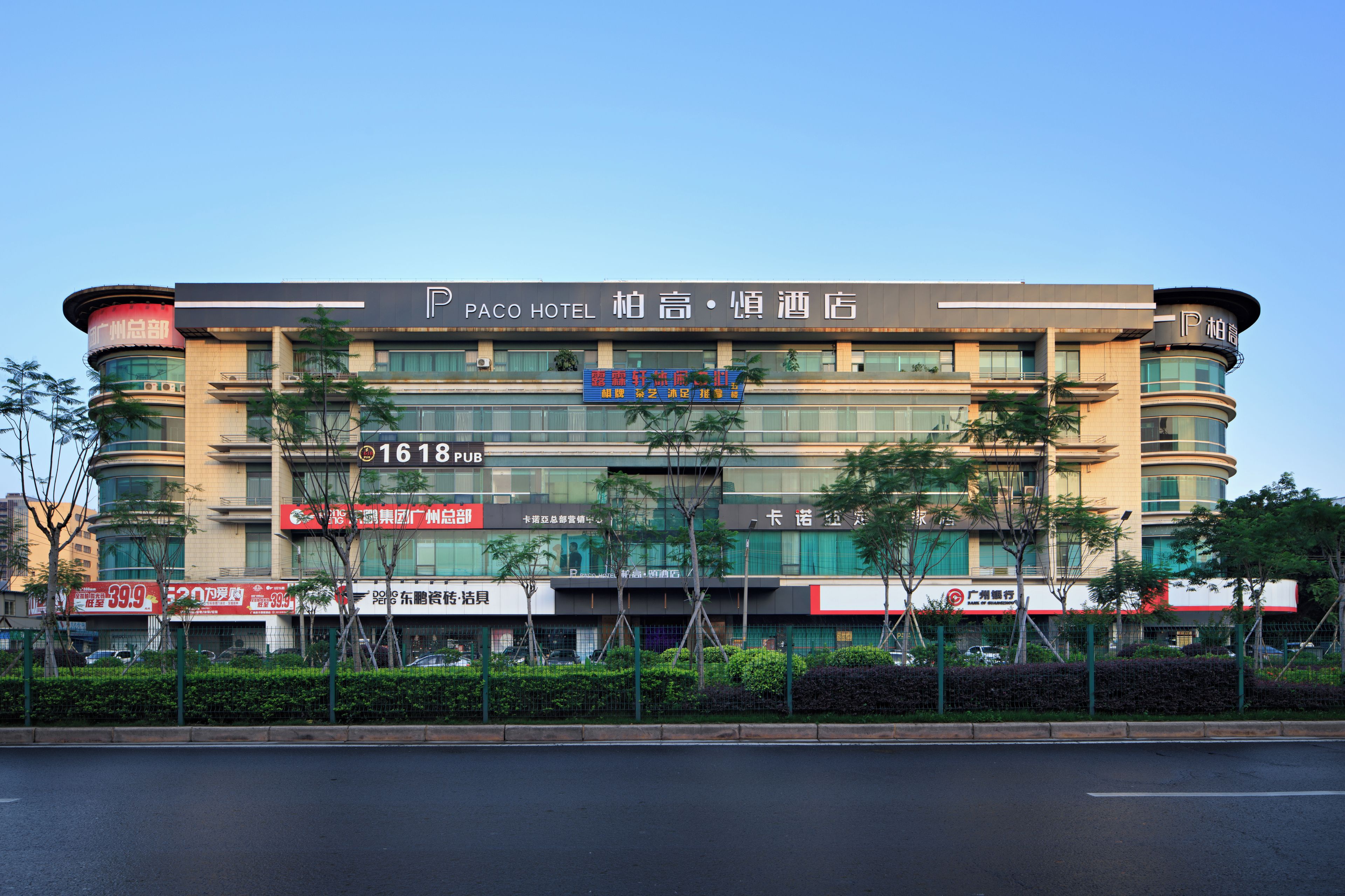 Ein mehrstöckiges Hotel mit einem gut sichtbaren 'PACO HOTEL' Schild, einem Restaurant namens '1618 PUB' und verschiedenen Geschäften im Erdgeschoss.