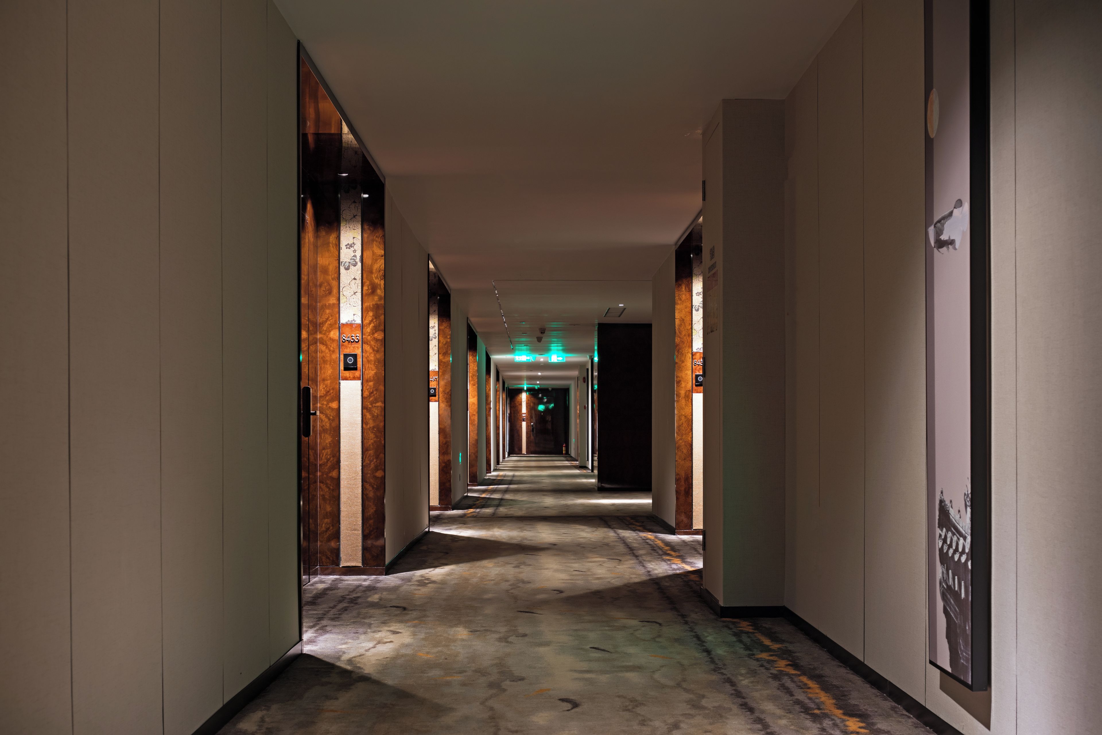 A hotel corridor with a carpeted floor, doors on both sides, and a ceiling with recessed lighting.